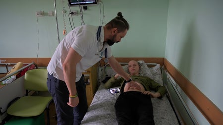 A doctor with a stethoscope checks a young male patient with cancer laying on a hospital bed