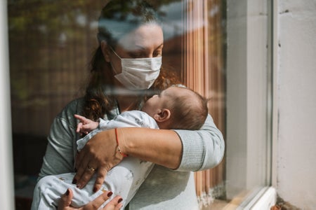 Mother with protective face mask holding her newborn baby