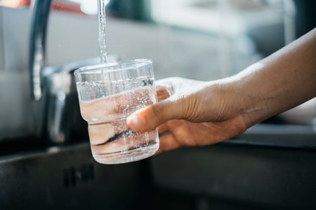 Woman's hand filling a glass with water at kitchen sink.