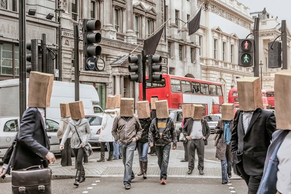 An commute scene with anonymous people all wearing paper bags on their heads while walking on a busy city street