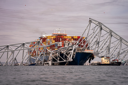 Container ship with orange and red cargo boxes resting behing metal beams of a collapsed bridge.